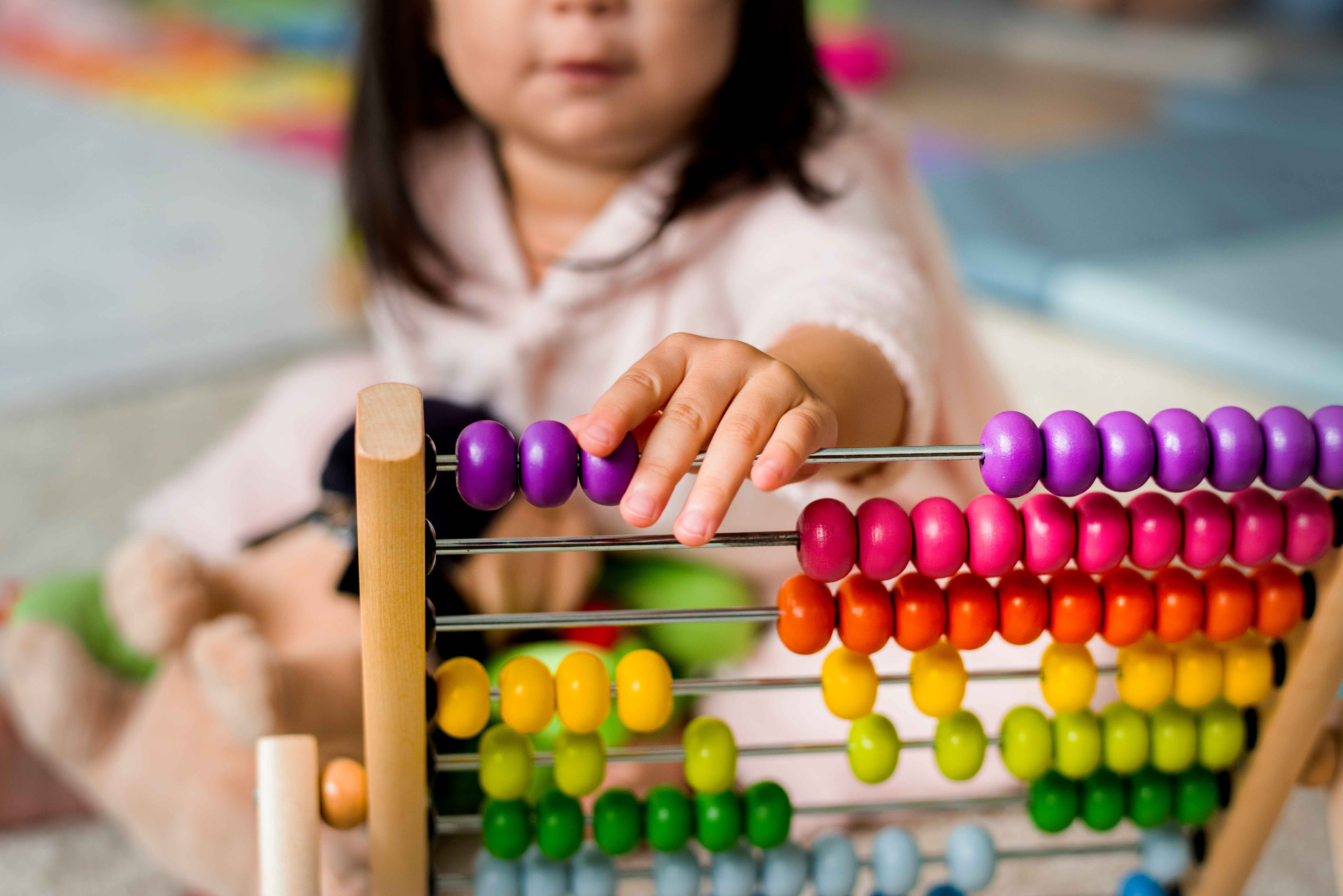 A young child playing with a colorful wooden abacus, moving the purple beads along the rods.