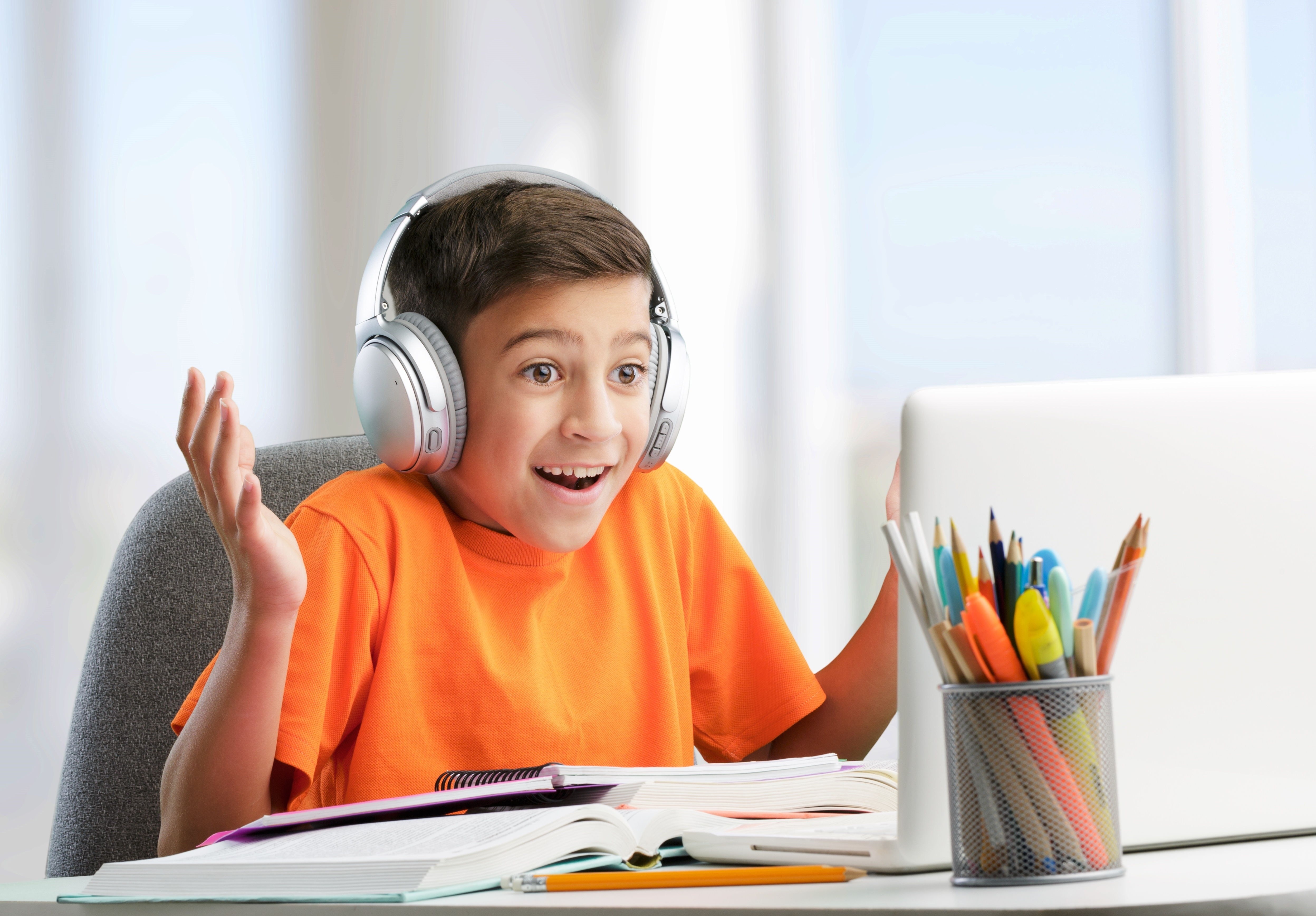 A young boy wearing headphones and smiling excitedly while attending an online class on his laptop, showing how engaging online learning and an English vocabulary class can be for children.